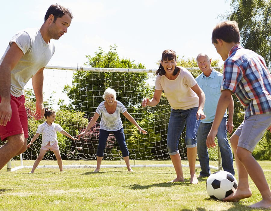 A young girl hugs a smiling woman from behind as they sit on a couch, both looking at each other happily in a bright, cozy living room.